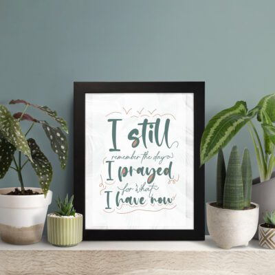 Christian wall art with the quote I Still Remember The Days I Prayed For What I Have Now in elegant cursive on a white background. displayed on the table in a black frame