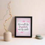 Christian wall art displaying We Walk By Faith Not By Sight with floral elements on a pale pink background. displayed on the wall in a black frame