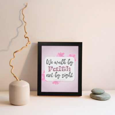 Christian wall art displaying We Walk By Faith Not By Sight with floral elements on a pale pink background. displayed on the wall in a black frame