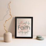 Christian wall art displaying the quote We Walk By Faith Not By Sight in elegant fonts on a soft beige-pink background. displayed on the wall in a black frame