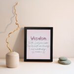 Christian wall art with the quote from Proverbs 2:6, featuring the word "Wisdom" in script on a soft pink background. displayed on the wall in a black frame