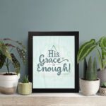 His Grace Is Enough Bible wall art with a mint background and teal script design, surrounded by decorative elements. displayed on the table in a black frame