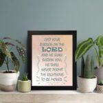 Cast Your Burden on the Lord Psalm 55:22 Bible verse wall art with teal lettering and soft peach background, Christian home decor. displayed on the table in a black frame