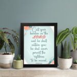 Cast Your Burden on the Lord Psalm 55:22 Christian wall art with teal and coral text on a mint green background with floral accents. displayed on the table in a black frame