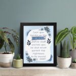 Christian wall art featuring Psalm 55:22 with navy blue text on a light blue and white background, decorated with blue flowers. displayed on the table in a black frame