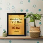 Infidu When You Can't Find The Sunshine Be The Sunshine wall art with a yellow background brown text and black frame hung on the table. perfect for inspiring positivity in any workspace