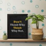 Infidu Don't Think Why, Think Why Not wall art with a black background yellow and white text, and a black frame on the table. Inspiring decor for home offices and workspaces.