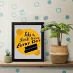 Infidu Take A Small Step Everyday wall art with a gray and yellow background black text and black frame on the table. Inspiring decor for any workspace.