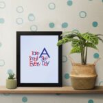 Infidu Take A Small Step Everyday wall art with a gray background navy blue and red text and a black frame on the table. Inspiring decor for any workspace.