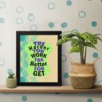 Infidu The Harder You Work The Better You Get wall art with a sandal-colored background green design, and a black frame on the table. Inspiring decor for home offices and workspaces.