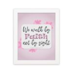 Christian wall art displaying We Walk By Faith Not By Sight with floral elements on a pale pink background. hung on the wall in a white frame