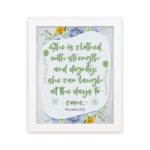 Christian wall art featuring Proverbs 31:25, with elegant script and floral accents in light green and gray background. hung on the wall in a white frame