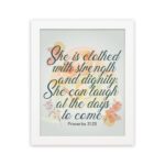 Christian wall art featuring the quote She is clothed with strength and dignity; she can laugh at the days to come from Proverbs 31:25, with an elegant design and pastel colors. hung on the wall in a white frame