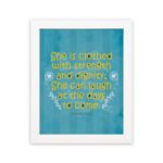 Christian wall art with Proverbs 31:25 verse in bold yellow text on a dark blue background with floral accents hung on the wall in a white frame