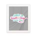 Infidu Take A Small Step Everyday wall art with a gray background and vibrant green, yellow, and pink text and white frame hung on the wall. Inspiring decor for any workspace.