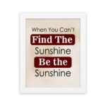 Infidu motivational wall art featuring the quote When You Can't Find the Sunshine Be the Sunshine on a white background with red text and a white frame hung on the wall. perfect for office decor.