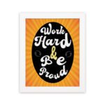 Work Hard Be Proud office wall art with white text on a black effect background gradient of orange and yellow, framed in white hanging on the wall. Perfect for home office decor.