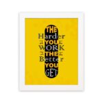 Infidu The Harder You Work The Better You Get wall art with a yellow background and dark yellow and white text with black shadow and white frame hung on the wall. Inspiring decor for home offices and workspaces.