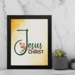 Jesus Christ text in green script with red floral accents on a glowing yellow-orange background, framed in black. displayed on the wall in a black frame