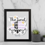 Bible wall art with The Lord Is My Rock, My Fortress, and My Deliverer in colorful pastel text on a light grey background with decorative elements. displayed on the wall in a black frame