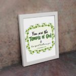 You Are The Temple Of God, His Spirit Dwells In You 1 Corinthians 3:16 Bible Verse Wall Art with green leaf wreath design. displayed on the wall in a white frame