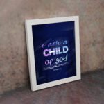 Infidu I Am A Child Of God wall art featuring soft glowing text in pink and blue on a dark blue background. displayed on the wall in a white frame