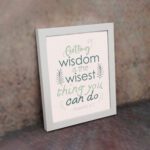 Infidu wall art with Proverbs 4:7 text surrounded by green leaves on a beige background. Elegant and minimal design. displayed on the wall in a white frame