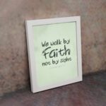 We Walk By Faith Not By Sight Bible Verse Wall Art on a mint green background. displayed on the wall in a white frame