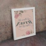 We Walk By Faith Not By Sight Christian Wall Art with pink roses and gray leaves on a soft pink background displayed on the wall in a white frame.