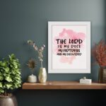 Bible wall art featuring The Lord Is My Rock, My Fortress, and My Deliverer in black handwritten-style lettering on a soft pink watercolor background. displayed on the wall in a white frame