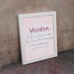 Christian wall art with the quote from Proverbs 2:6, featuring the word "Wisdom" in script on a soft pink background. displayed on the wall in a white frame