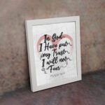 In God I Have Put My Trust, I Will Not Fear Psalm 56:4 Bible Verse Wall Art with pink watercolor arc and black frame. displayed on the table in a white frame