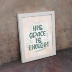 Christian wall art featuring the phrase His Grace Is Enough in teal lettering on a soft pink background with decorative swirls. displayed on the wall in a white frame