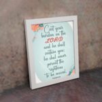 Cast Your Burden on the Lord Psalm 55:22 Christian wall art with teal and coral text on a mint green background with floral accents. displayed on the wall in a white frame