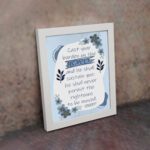 Christian wall art featuring Psalm 55:22 with navy blue text on a light blue and white background, decorated with blue flowers. displayed on the wall in a white frame