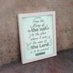 Wall art displaying Psalm 113:3 with elegant cursive font and leafy motifs on a mint green background. displayed on the wall in a white frame