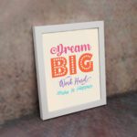 Infidu Dream Big Work Hard Make It Happen wall art with a light pink background and vibrant pink, orange, violet, and sky blue text and a white frame on the wall. Inspiring decor for home offices and workspaces.