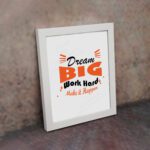 Infidu Dream Big Work Hard Make It Happen wall art with a gray background black and orange text and a white frame on the wall. Inspiring decor for home offices and workspaces.