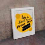 Infidu Take A Small Step Everyday wall art with a gray and yellow background black text and white frame on the wall. Inspiring decor for any workspace.