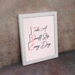 Infidu Take A Small Step Everyday wall art with a gray and light pink background black and red text and a white frame on the wall. Inspiring decor for any workspace.