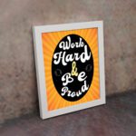 Work Hard Be Proud office wall art with white text on a black effect background gradient of orange and yellow, framed in white on the wall. Perfect for home office decor.