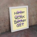 Infidu The Harder You Work The Better You Get wall art with a light sandal background and dark blue and violet text and white frame on the wall. Inspiring decor for home offices and workspaces.