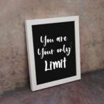 Infidu motivational quotes wall art featuring You Are Your Only Limit on a dark black background and white frame on the wall. Perfect for inspiring your workspace.