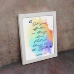 Bible wall art featuring Colossians 3:2 in cursive text on a colorful rainbow background. displayed on the wall in a white frame