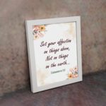 Infidu Bible wall art with Colossians 3:2 in dark brown text, surrounded by peach and beige flowers on a cream background. displayed on the wall in a white frame