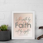 Christian wall art displaying the quote We Walk By Faith Not By Sight in elegant fonts on a soft beige-pink background. displayed on the wall in a white frame