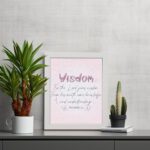 Christian wall art with the quote from Proverbs 2:6, featuring the word "Wisdom" in script on a soft pink background. displayed on the table in a white frame