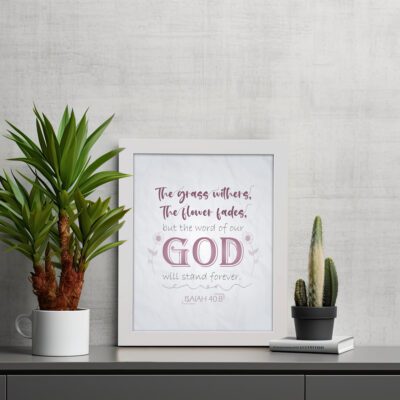 Christian wall art with the verse The Grass Withers, The Flower Fades But The Word Of Our God Will Stand Forever Isaiah 40:8. displayed on the table in a white frame