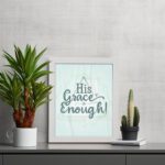 His Grace Is Enough Bible wall art with a mint background and teal script design, surrounded by decorative elements. displayed on the table in a white frame