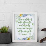 Christian wall art featuring Proverbs 31:25, with elegant script and floral accents in light green and gray background. displayed on the wall in a white frame